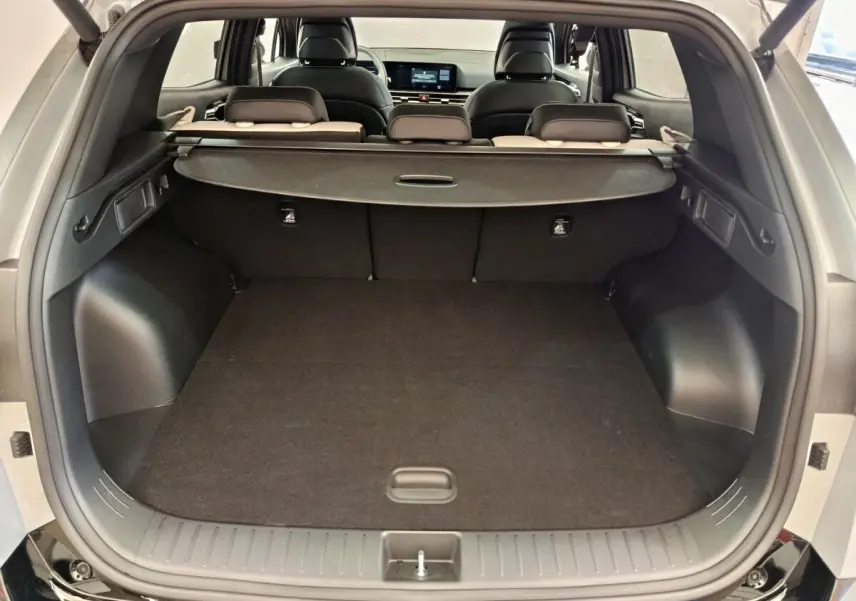 Coffre ouvert du Kia Sportage gris foncé vu de l'arrière, avec cache-bagages et sièges arrière rabattables visibles.