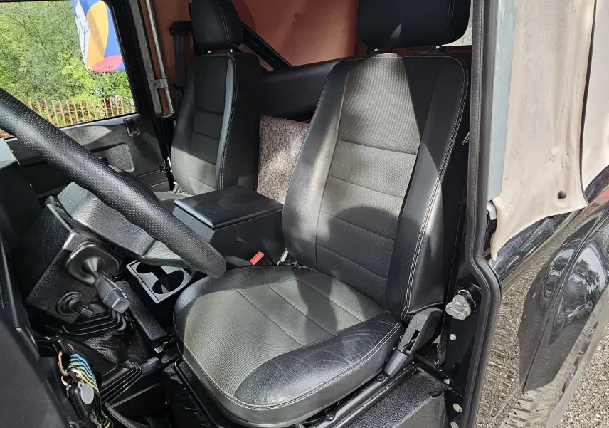 Vue intérieure côté conducteur du Land Rover Defender 90 noir avec sièges en cuir et capote beige souple.