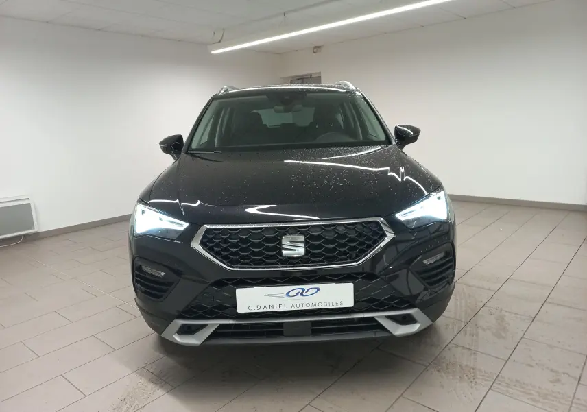 Vue avant d'un SEAT Ateca 2.0 TDI 150 DSG7 Copa noir Magic Nacré avec phares allumés dans un showroom.