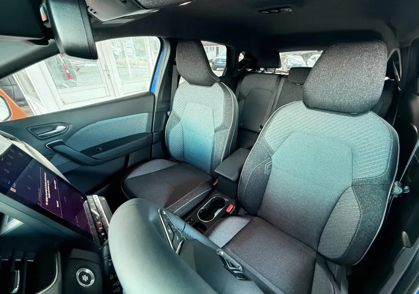 Intérieur du Renault Captur E-Tech 2025, vue avant des sièges tissu gris avec détails bleus, tableau de bord et console centrale visibles.