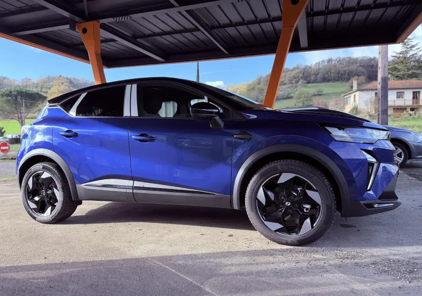 Profil côté gauche du Renault Captur E-Tech hybride 2025 en bleu Iron Metal avec toit noir sous abri.