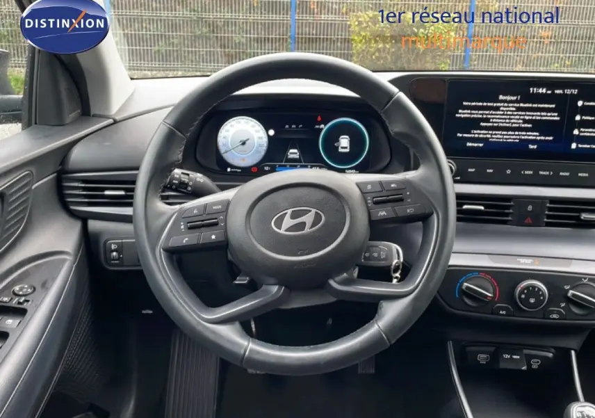 Vue intérieure centrée sur le volant cuir et le tableau de bord numérique de la Hyundai i20 noire Phantom Metal 2025.