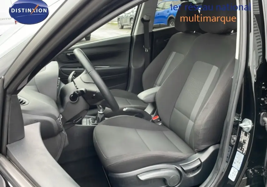 Intérieur côté conducteur d'une Hyundai i20 noire, montrant les sièges en tissu gris et le volant multifonction.