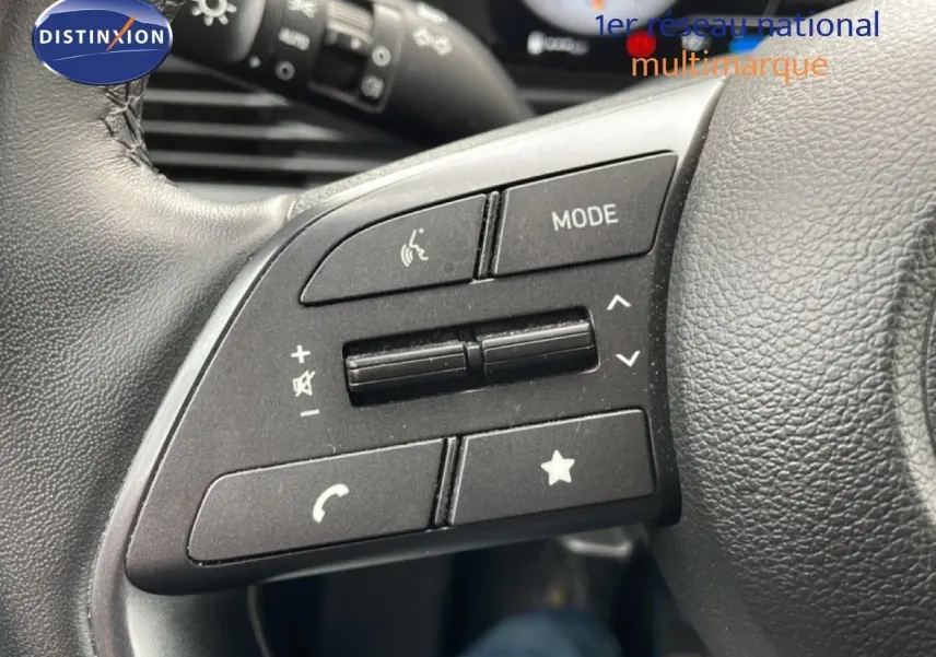 Gros plan sur les commandes au volant côté gauche d'une Hyundai i20 noire Phantom Metal 2025, boutons multifonctions visibles.