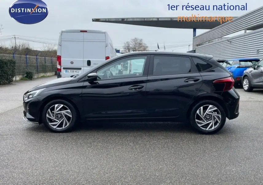 Profil côté gauche d'une Hyundai i20 noire Phantom Metal 2025 garée sur un parking extérieur.
