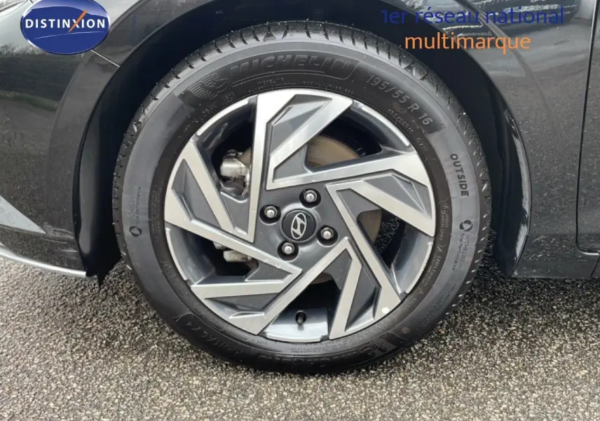 Gros plan sur la roue avant droite d'une Hyundai i20 noire Phantom Metal avec jante alliage au design géométrique.