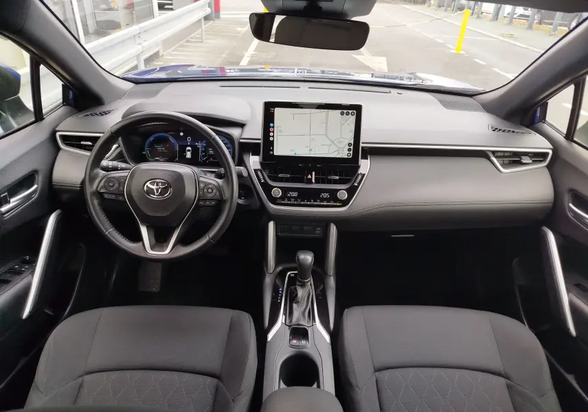 Vue intérieure avant de la Toyota Corolla Cross 1.8l 140h Dynamic 2024, tableau de bord gris avec écran tactile central et volant multifonction.
