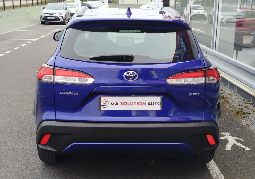 Vue arrière d'une Toyota Corolla Cross 1.8l 140h Dynamic en bleu cosmique, avec feux LED et logo hybride visible.