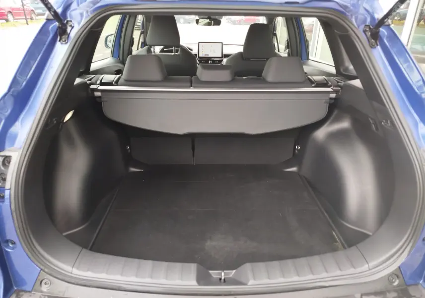 Coffre ouvert d’une Toyota Corolla Cross 1.8l 140h Dynamic bleu cosmique, vue arrière montrant l’espace de chargement et l’intérieur gris.