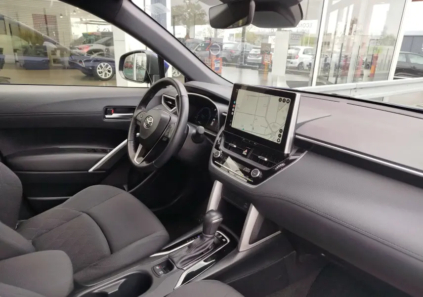 Intérieur de la Toyota Corolla Cross 2024 vue côté conducteur, tableau de bord noir avec écran tactile et boîte auto.