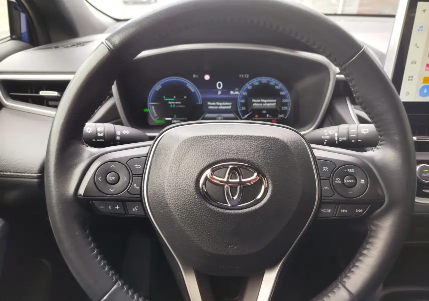 Vue rapprochée du volant noir de la Toyota Corolla Cross 2024 avec tableau de bord numérique et commandes intégrées.