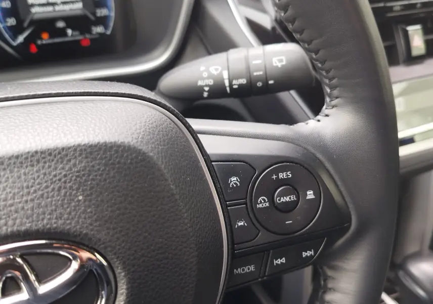 Gros plan sur le volant noir de la Toyota Corolla Cross 2024, montrant les commandes de régulateur et d’aide à la conduite.