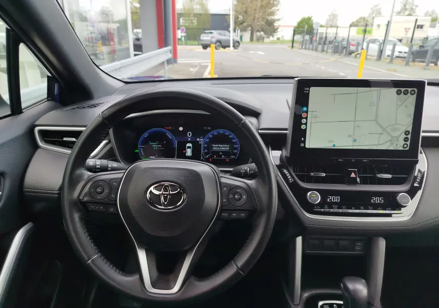 Vue intérieure centrée sur le volant et le tableau de bord numérique de la Toyota Corolla Cross 2024, avec écran tactile affichant une carte.