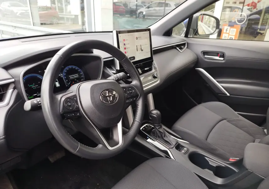 Intérieur de la Toyota Corolla Cross 1.8l 140h Dynamic 2024, vue côté conducteur, tableau de bord et écran tactile central.