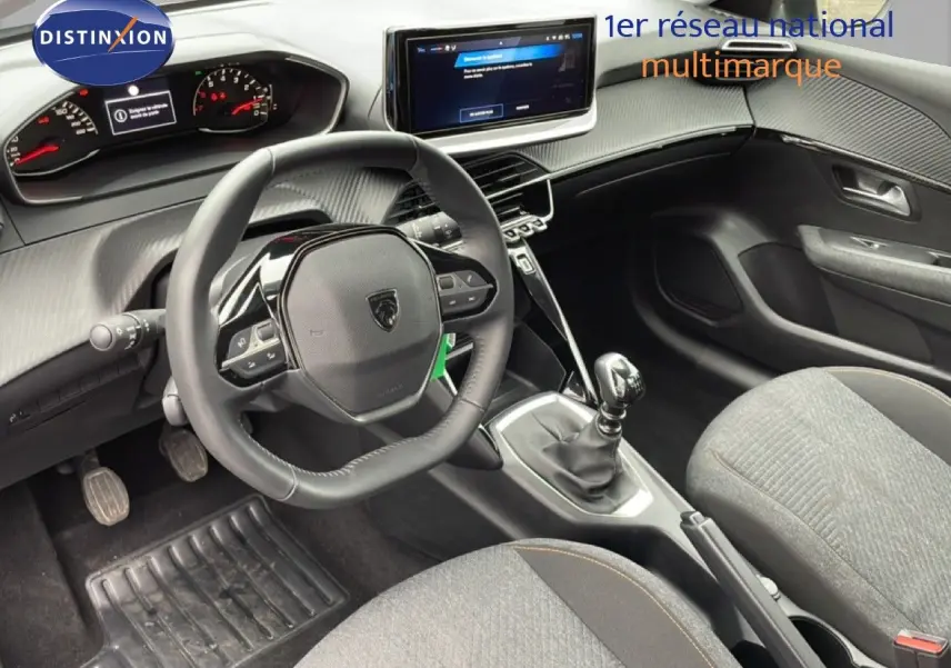 Intérieur de Peugeot 208 2025 vu côté conducteur, volant cuir multifonction, console centrale avec boîte manuelle et écran tactile.