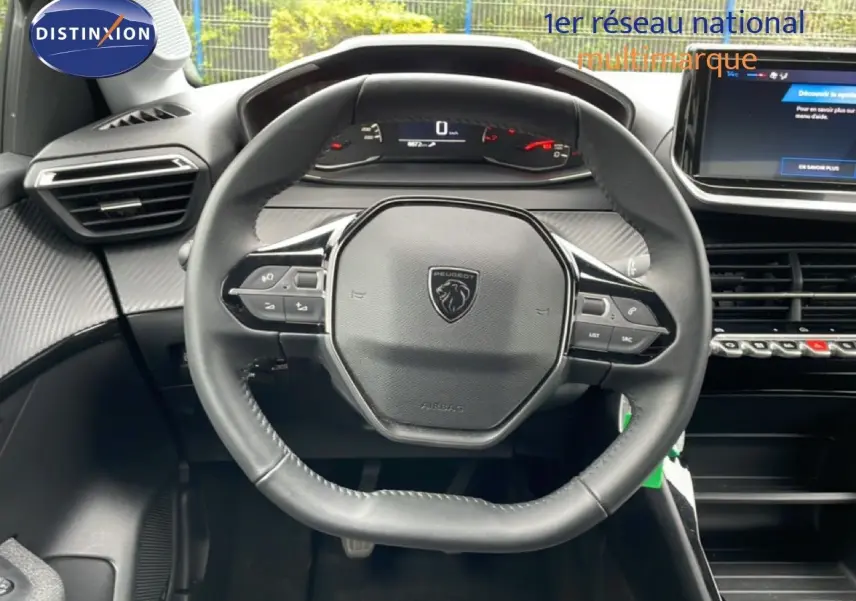 Vue rapprochée du volant cuir multifonction noir de la Peugeot 208 1.2 100CH STYLE, avec tableau de bord digital en arrière-plan.