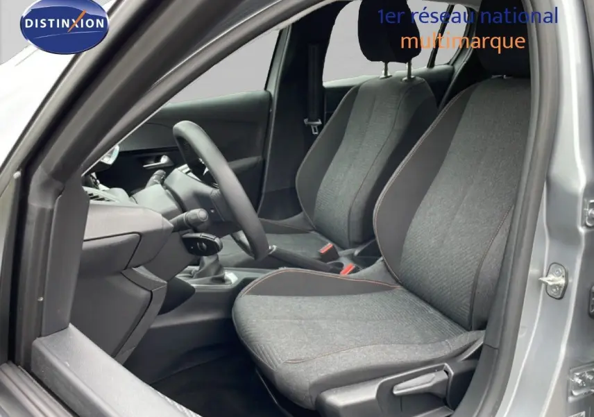 Vue intérieure côté conducteur de la Peugeot 208 gris Artense métal, sièges tissu gris avec surpiqûres orange.