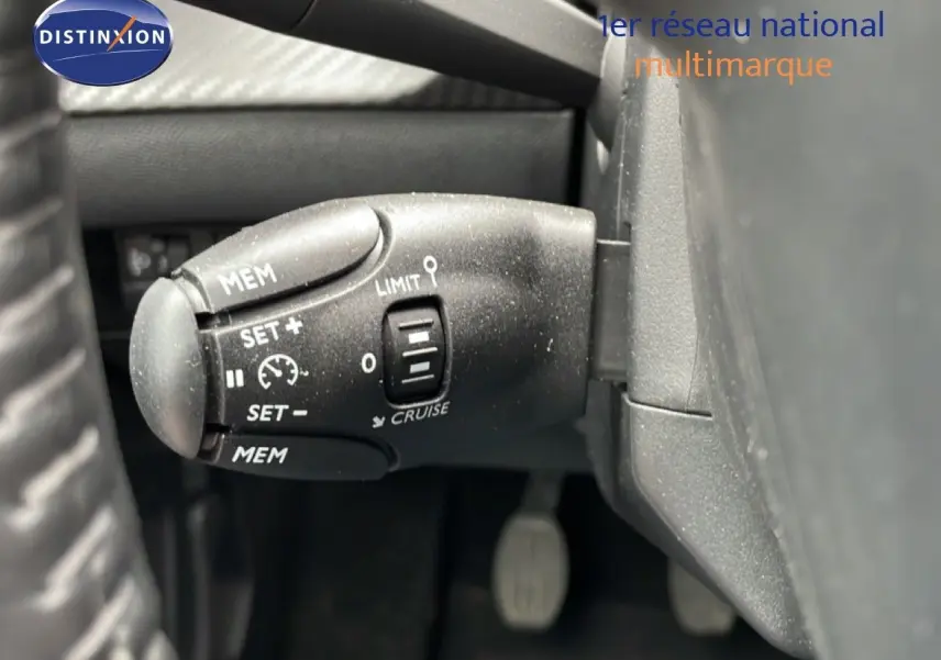 Gros plan sur la commande de régulateur de vitesse à gauche du volant dans l’habitacle d’une Peugeot 208 gris Artense.