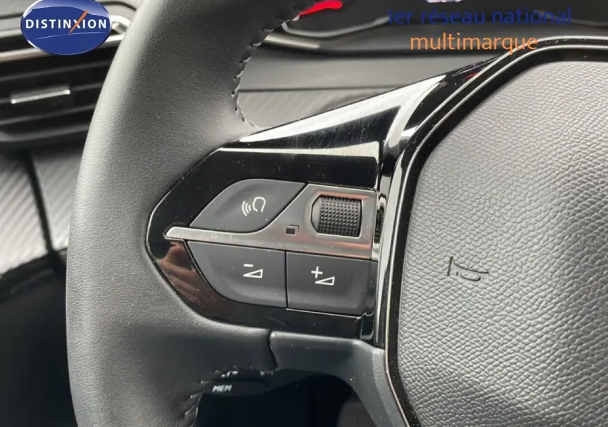 Gros plan sur le volant noir de la Peugeot 208 2025 avec commandes audio intégrées et finition brillante.
