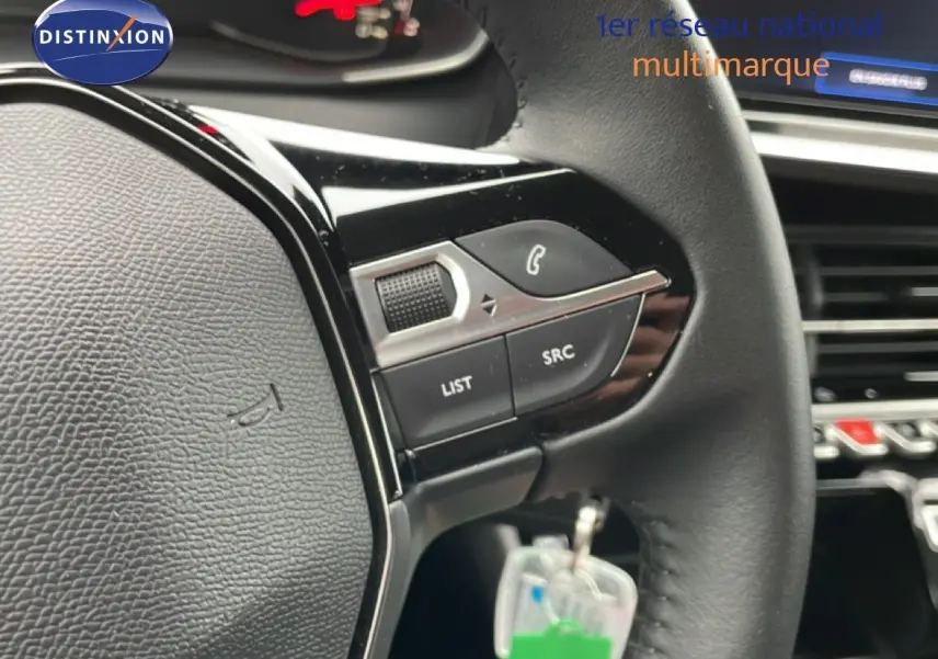 Gros plan sur le volant noir de la Peugeot 208 2025 avec commandes intégrées et tableau de bord en arrière-plan.