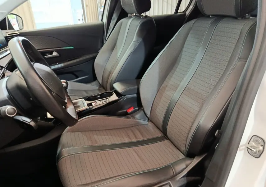 Vue intérieure côté conducteur de la Peugeot 208 blanche, mettant en valeur les sièges tissu et cuir gris avec surpiqûres vertes.