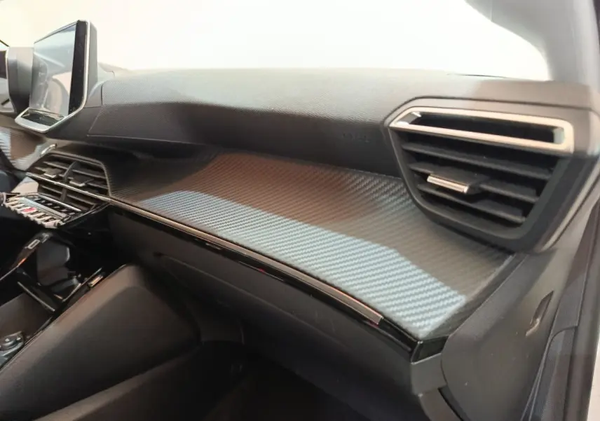 Vue intérieure côté passager du tableau de bord noir avec insert effet carbone du Peugeot 208 PureTech 100 S&S Allure Business.