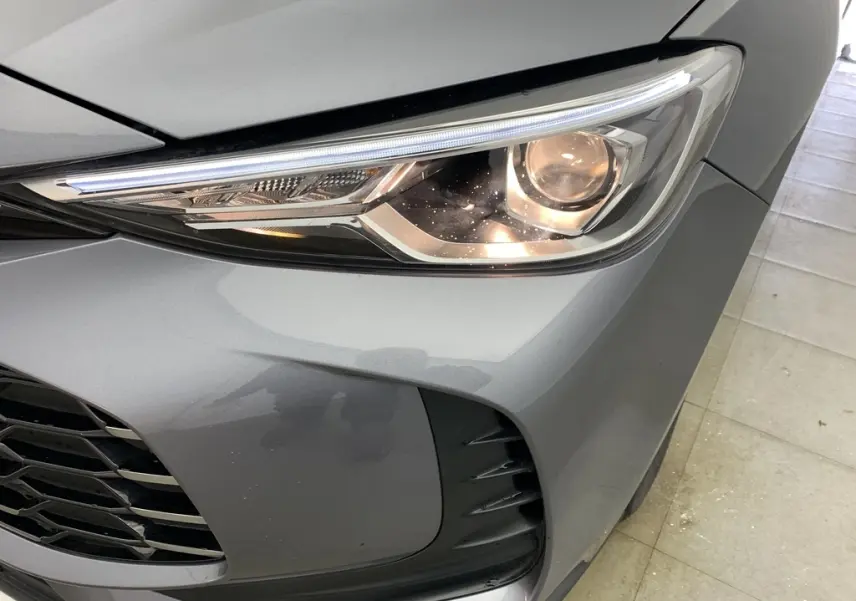 Gros plan sur le phare avant droit du MG ZS 1.5 L Hybrid+ 2026 en gris Hampstead avec calandre et prise d'air noire.