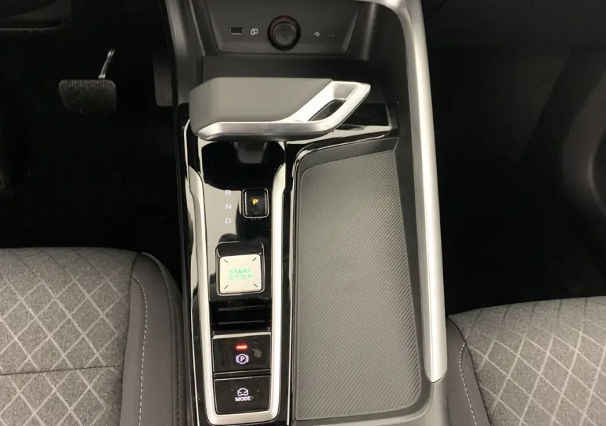 Vue plongeante sur la console centrale noire brillante du MG ZS 1.5 L Hybrid+ avec levier de vitesse et bouton start/stop.