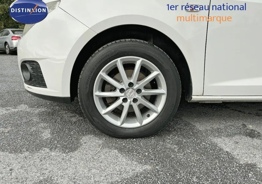 Gros plan sur la roue avant gauche d'une SEAT Ibiza blanche 2010, mettant en valeur la jante alliage et le passage de roue.