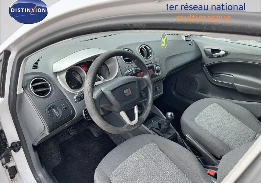 Intérieur de la SEAT Ibiza 1.6 TDI 90CH STYLE 2010 blanche, vue côté conducteur montrant volant, tableau de bord et sièges gris.