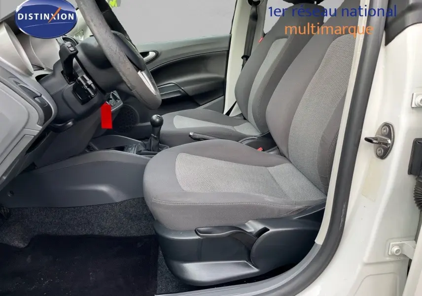Vue intérieure côté conducteur d'une SEAT Ibiza blanche 2010 avec sièges gris et boîte manuelle visible.