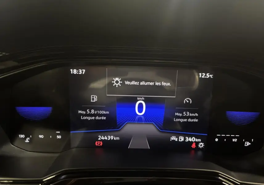 Tableau de bord numérique du Volkswagen Taigo 2023 affichant vitesse, consommation et alertes, vue frontale rapprochée.