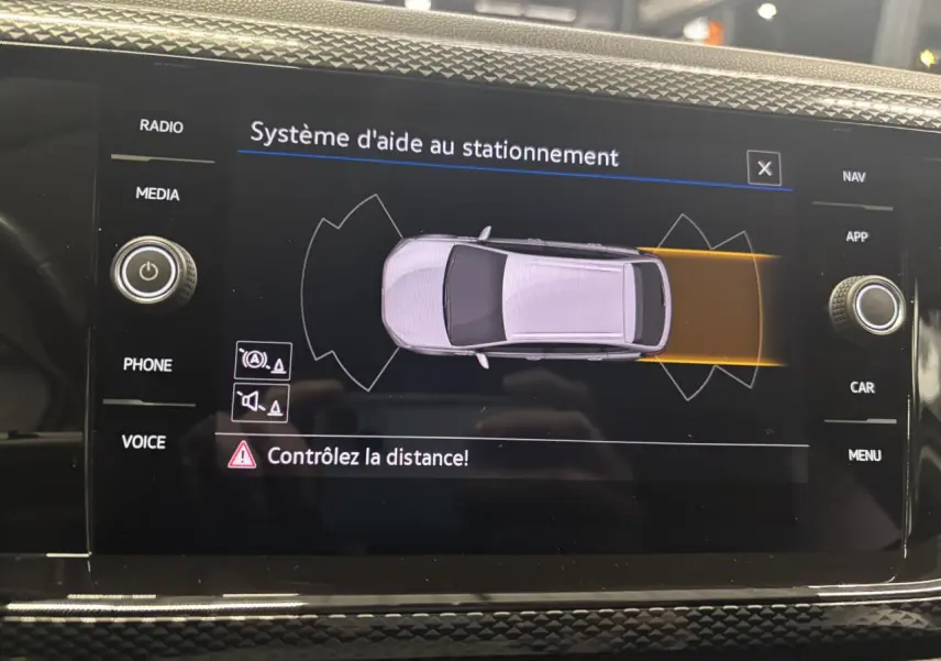 Écran tactile intérieur du Volkswagen Taigo blanc montrant le système d'aide au stationnement vue de dessus du véhicule.