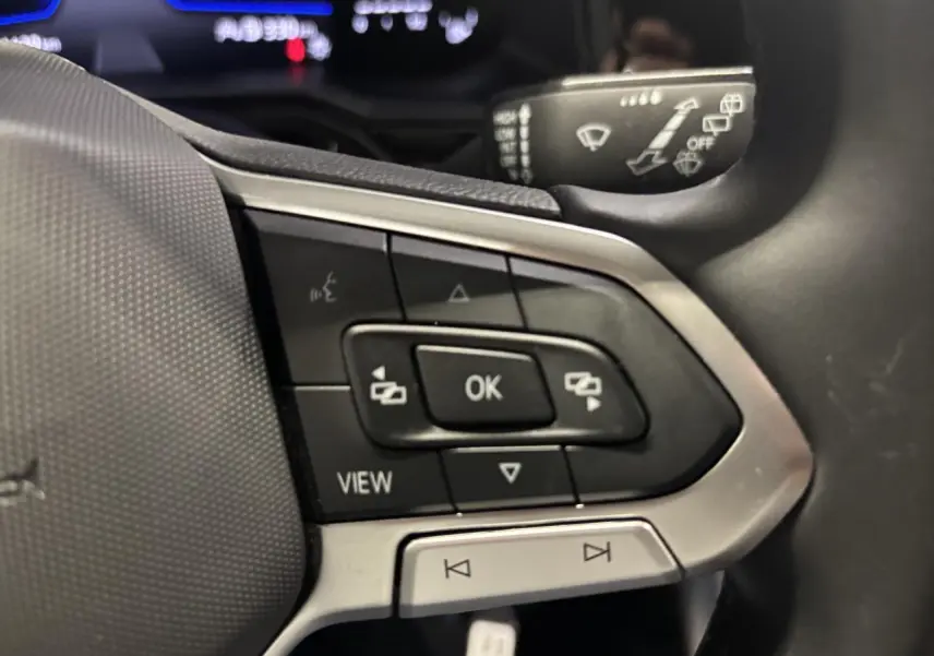 Gros plan sur les commandes multifonctions du volant cuir du Volkswagen Taigo blanc, avec boutons de navigation et vue.