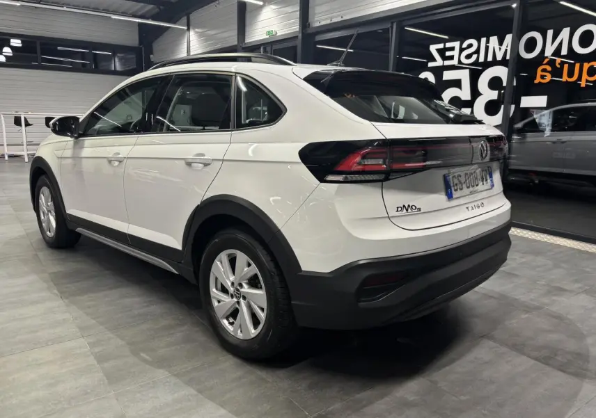 Vue 3/4 arrière droite du Volkswagen Taigo blanc avec jantes alliage et feux arrière LED dans un showroom.