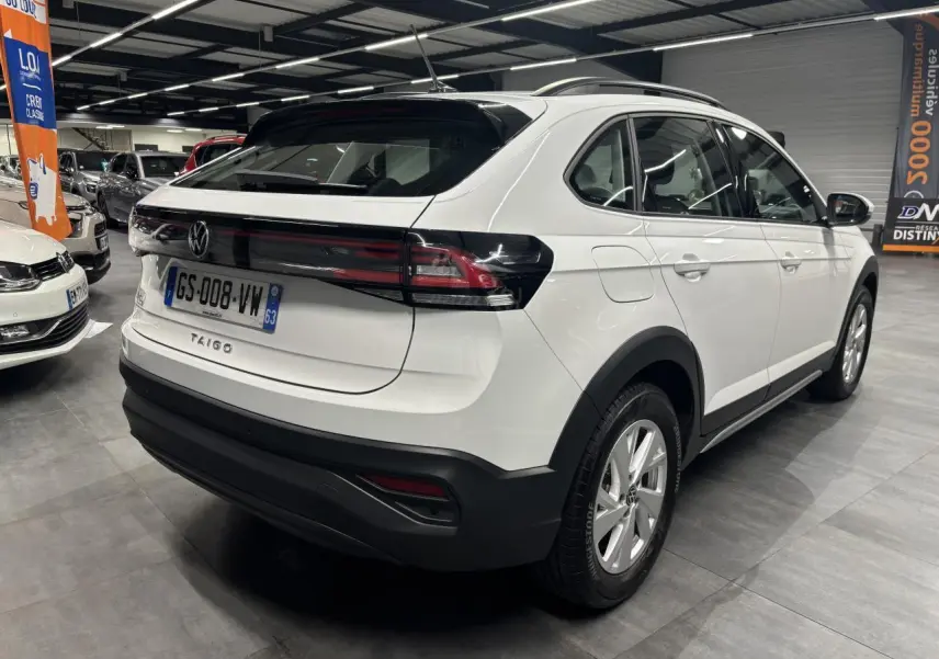 Vue 3/4 arrière droite d'un Volkswagen Taigo blanc avec feux arrière noirs et jantes alliage en showroom.