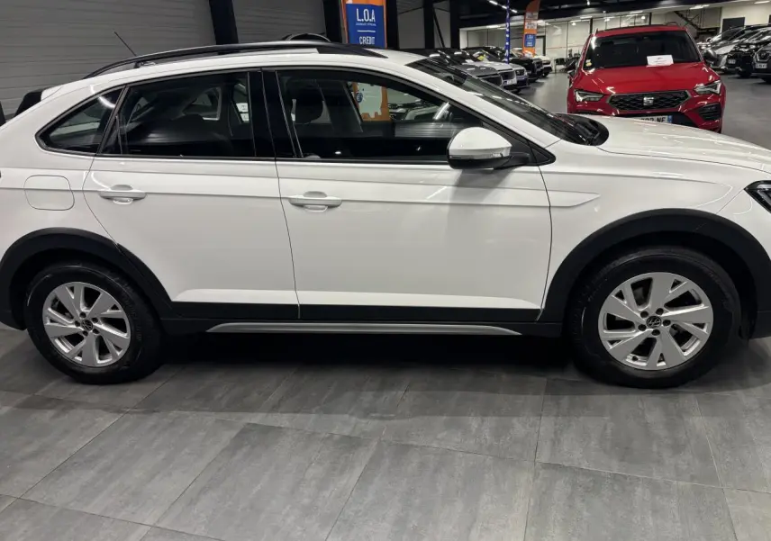 Vue de profil côté gauche d'un Volkswagen Taigo blanc 2023 avec jantes alliage et protections noires sur les passages de roues.