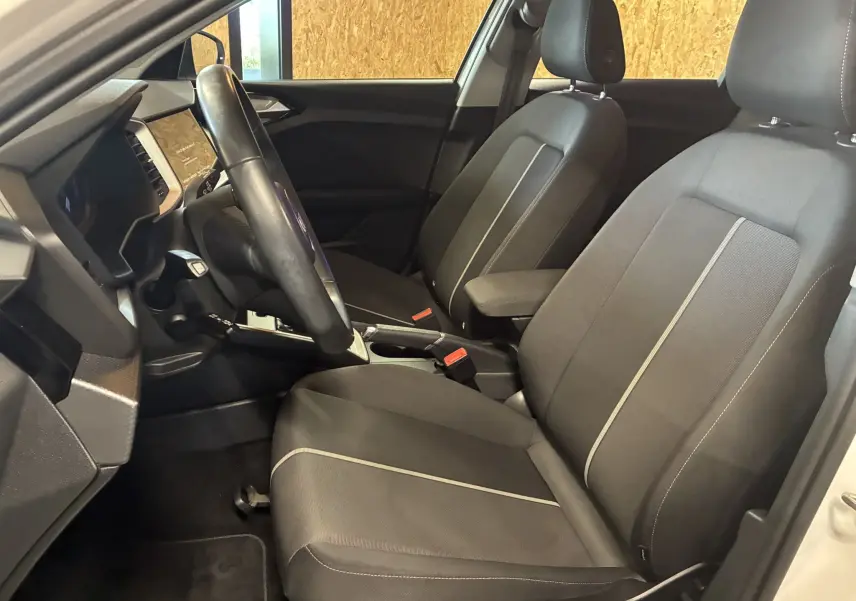 Vue intérieure côté conducteur de l'Audi A1 2022 avec sièges tissu noirs et volant cuir multifonctions.