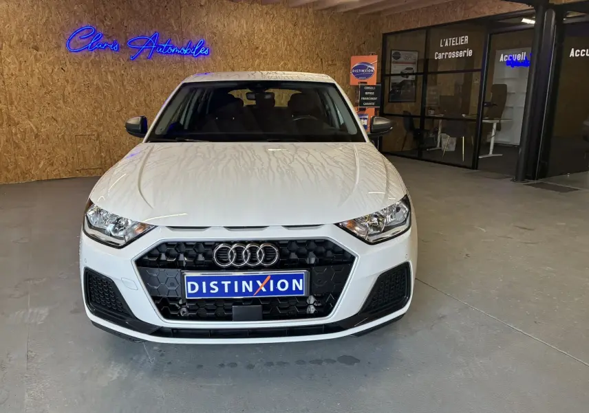 Audi A1 blanche vue de face en intérieur, avec calandre noire hexagonale et logo Audi bien visible.