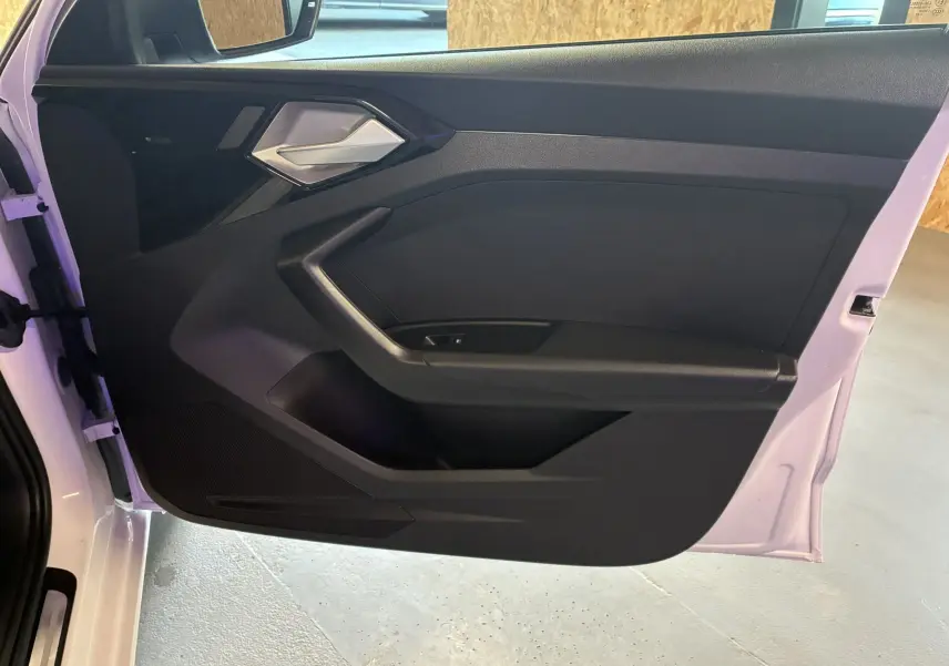Vue intérieure de la porte avant gauche noire avec poignée argentée d'une Audi A1 blanche 2022.