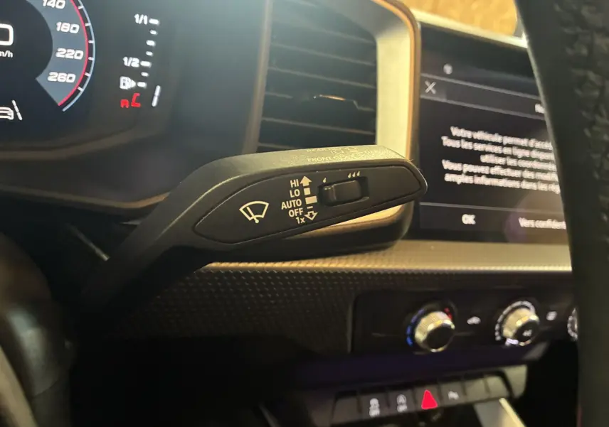 Gros plan sur la commande d'essuie-glace à gauche du volant dans l'habitacle noir de l'Audi A1 blanche de 2022.