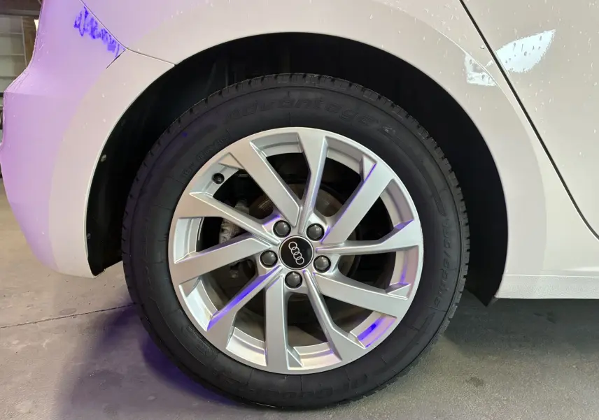 Gros plan sur la roue arrière droite d'une Audi A1 blanche avec jante alu 17 pouces et logo Audi au centre.