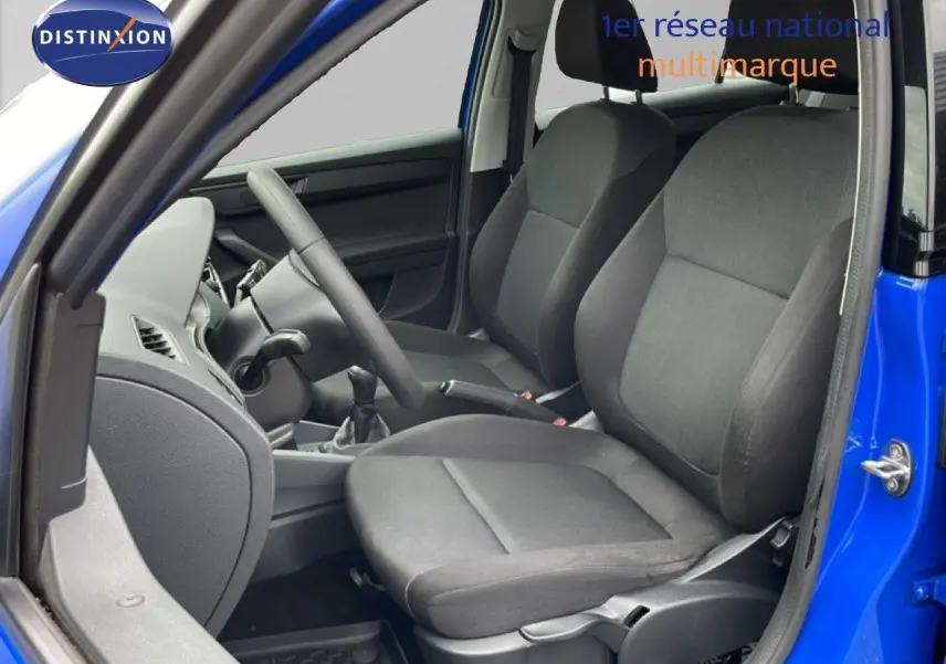 Vue intérieure côté conducteur de la Skoda Fabia 1.0 TSI bleu énergie avec sièges tissu noirs et volant visible.