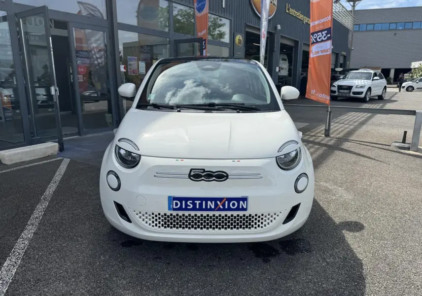 Vue frontale d'une Fiat 500 électrique blanche 2022 avec toit panoramique, stationnée devant un garage.