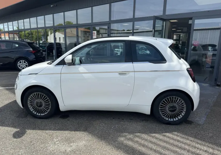 Profil côté gauche d'une Fiat 500 électrique blanche 2022 avec jantes alliage 16'' et toit panoramique visible.