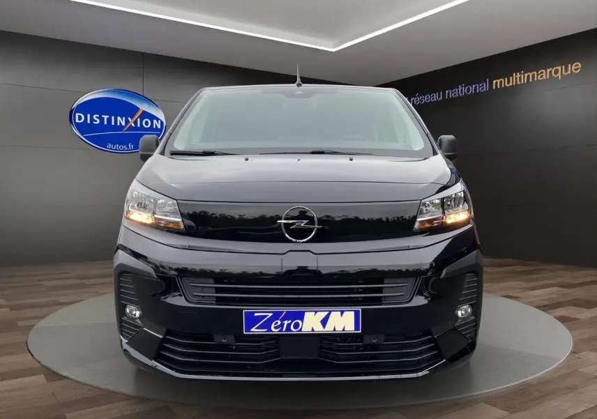 Vue frontale d'un Opel Vivaro noir 2025 avec feux allumés et plaque Zéro KM dans un showroom.
