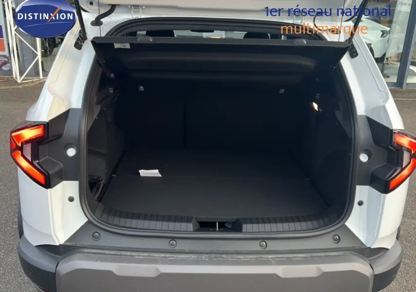 Coffre ouvert vu de l'arrière d'un Dacia Duster Hybrid 140 Journey blanc Glacier avec feux arrière LED en forme de Y.