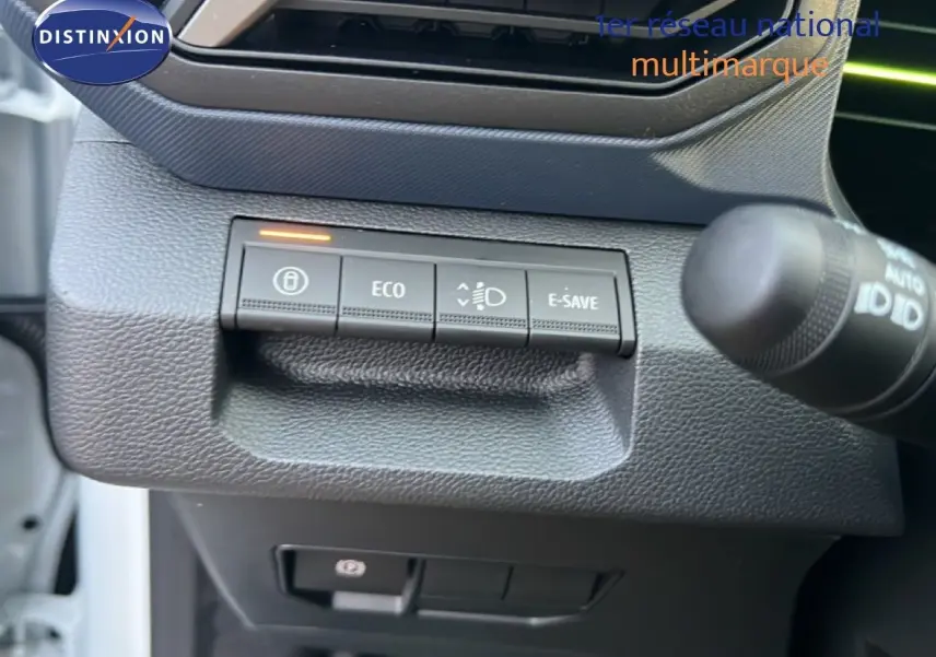 Gros plan sur les commandes de mode de conduite et feux du Dacia Duster Hybrid 140 blanc Glacier, côté gauche du tableau de bord.