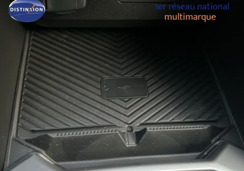 Gros plan sur le chargeur smartphone sans fil noir dans le coffre central du Dacia Duster Hybrid 140 Journey blanc glacier.