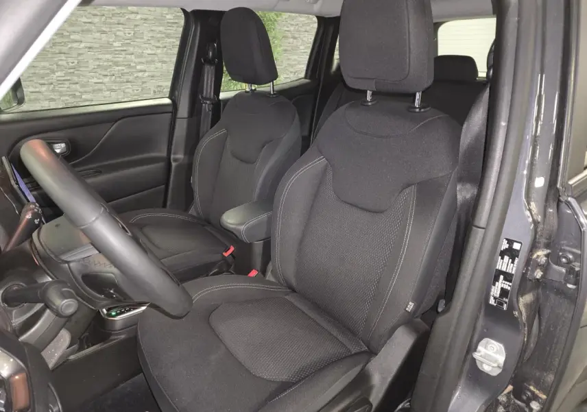 Vue intérieure côté conducteur du Jeep Renegade gris, sièges tissu noir avec accoudoir central et volant visible.